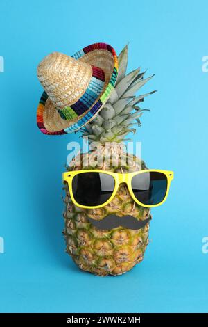 Pineapple with Mexican sombrero hat, sunglasses and fake mustache on light blue background Stock Photo