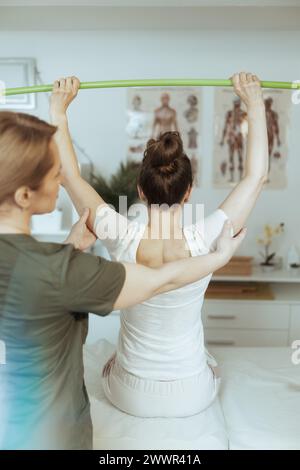 Healthcare time. Seen from behind female medical massage therapist in massage cabinet with client doing checkup. Stock Photo