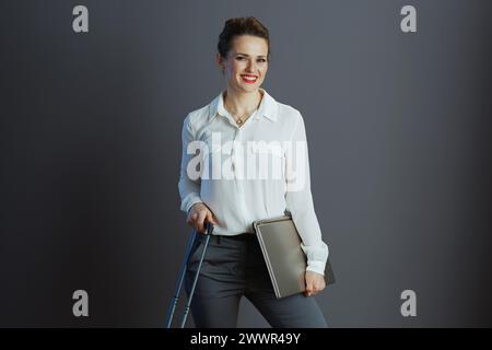 smiling modern business woman in white blouse with laptop and wheel bag isolated on gray. Stock Photo