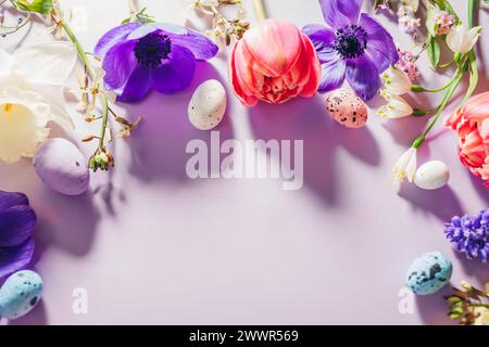 Happy Easter mockup. Easter eggs with spring pink purple flowers flat lay on purple background. Greeting card or banner frame with blooms. Space. Top Stock Photo