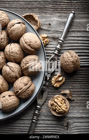 Walnut nuts and kernels in blue plate with a vintage silver nut cracker on old grunge wooden table close up. Food photography Stock Photo
