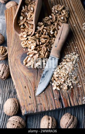 Crushed walnut nuts kernels and knife on wooden plate close up. Food photography Stock Photo