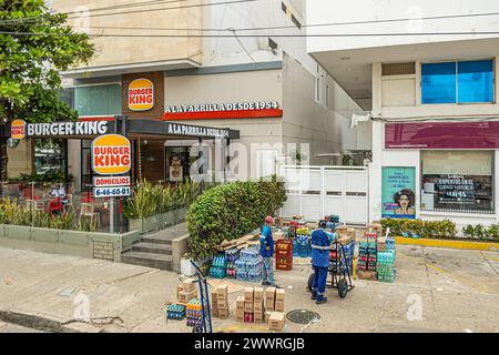 Cartagena, Colombia - July 25, 2023: Central Bocagrande Carrera 2. Burger king fast food restaurant. 2 delivery workers with collection of drink cases Stock Photo