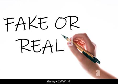 Children hand with pen write on an blue white background. Writing hand. Word Fake or real Stock Photo