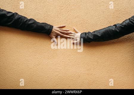 Two hands, belonging to different individuals, gently touching each other against a plain wall. Stock Photo