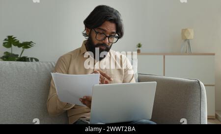 Arabian Indian man working from home talk video call with laptop discuss documents financial papers utility bills business loan insurance male Stock Photo