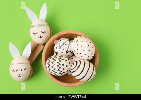Wooden spoons and bowl with painted Easter eggs on green background Stock Photo
