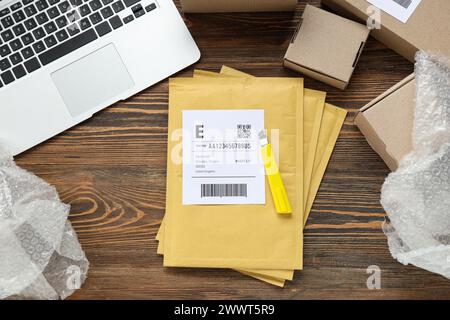 Envelopes with label, utility knife, laptop and cardboard packages on wooden table Stock Photo