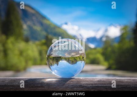 Wildbach in den Bergen mit Alpenpanorama im Hintergrund spiegelt sich in einer Glaskugel. Schmelzwasser führende Wildbäche in den Alpen wie zum Beispiel die Breitachklamm sind eine interessante Sehenswürdigkeit und beliebtes Ausflugsziel - auch an Tagen mit schlechtem Wetter. Es gibt verschiedene Wandertouren entlang solcher Gewässer die dann teils über Stege entlang von Stromschnellen und kleinen Wasserfällen führen. Raum Oberstdorf Bayern Deutschland *** Torrent in the mountains with a panoramic view of the Alps in the background reflected in a glass sphere Torrents carrying meltwater in the Stock Photo