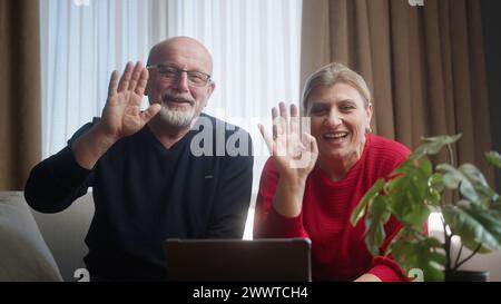 Elderly family sitting on the couch looking into the camera, using webcam to talking with grandchildren or adult children. Webcam view, video chat and Stock Photo
