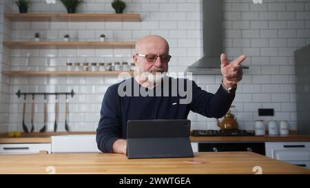 Elderly man sit in kitchen enter credit card number on tablet and due insufficient funds experiencing problems during payment online with credit card Stock Photo