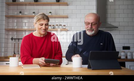 Senior retired couple sit in kitchen doing paperwork, checking calculating bills bank loan payment, discuss unpaid debt taxes. Old grandparents family Stock Photo