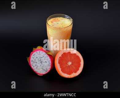Freshly squeezed grapefruit and pitaya juice in a tall faceted glass on a black background. Close-up. Stock Photo