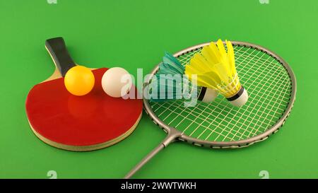 Table tennis racket with a yellow ball and a white ball on it and badminton racket with a feather shuttlecock on clear green background Stock Photo