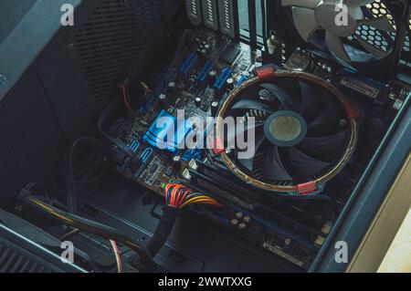 A close-up view of the inside of a broken desktop computer case, showing a computer motherboard, CPU fan, and its components. Stock Photo