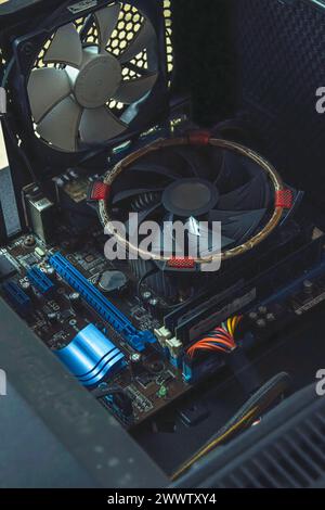 A close-up view of the inside of a broken desktop computer case, showing a computer motherboard, CPU fan, and its components. Stock Photo