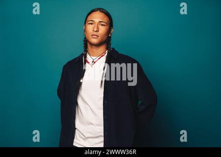 This young man exudes self-confidence standing in the studio. With long braided hair and stylish jewelry, including a necklace, he exudes ethnic pride Stock Photo