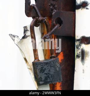 Old closed padlock hanging on the hinges Stock Photo