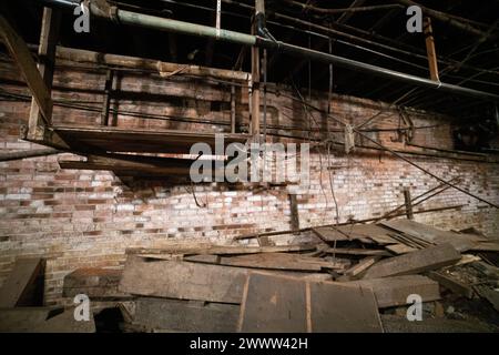 A suspended wooden platform hangs above fallen planks and debris along an old brick wall in the Seattle Underground, Washington. Stock Photo