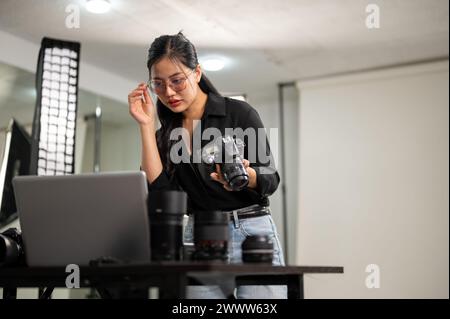 An attractive, professional Asian female photographer is checking images on her laptop, working in a studio. Stock Photo