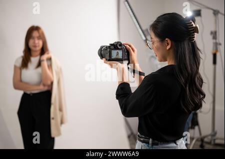A professional, cool Asian female photographer taking pictures of a model in the studio with professional lighting equipment. A team of fashion photos Stock Photo