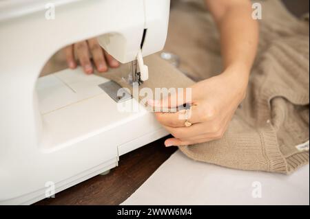 A close-up image of a female tailor is sewing a dress with a sewing machine, working in her studio. fashion designer, seamstress, dressmaker Stock Photo