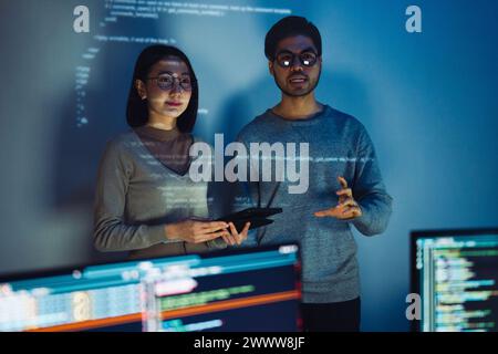 two asian and indian developer presentation about coding software data with devops team at night in office Stock Photo