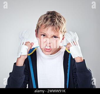 Portrait, angry and boy with fist, child and expression with frustrated on grey studio background. Face, bully and kid with forks for claws and Stock Photo