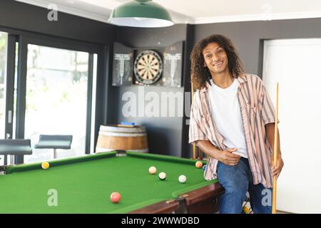 A young African American man with curly hair stands by a pool table with copy space Stock Photo