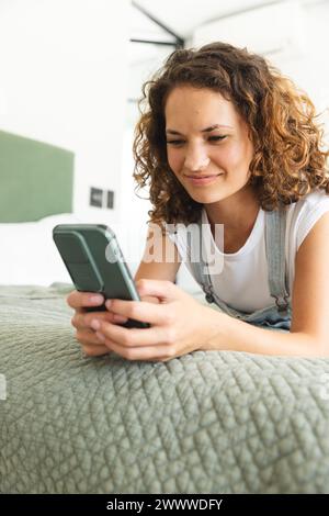 A young Caucasian woman is engaged with her smartphone on bed at home Stock Photo