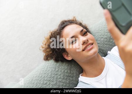 A young Caucasian woman is taking a selfie on bed at home Stock Photo