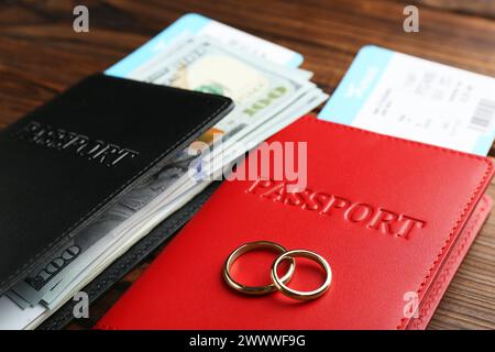 Honeymoon concept. Two golden rings, passports, money and tickets on wooden table, closeup Stock Photo