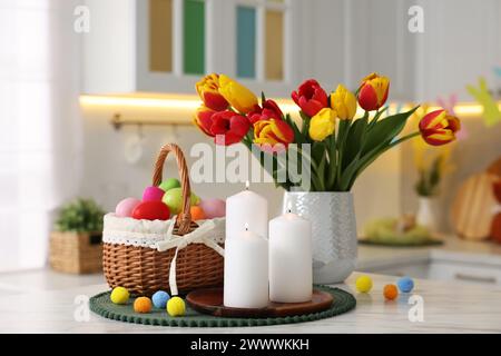 Easter decorations. Bouquet of tulips, painted eggs and burning candles on table indoors, closeup Stock Photo