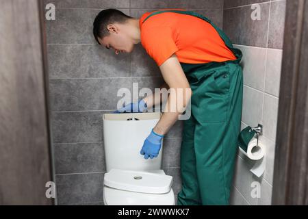 Young plumber repairing toilet bowl in water closet Stock Photo