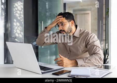 Upset and disappointed businessman at workplace got negative financial results, unsatisfied man working inside office at workplace with laptop. Stock Photo