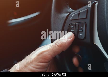 Driver pushing volume down button on car steering wheel, selective focus Stock Photo