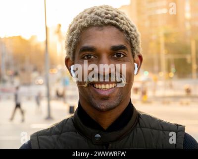 Portrait of a young smiling African American man with mini wireless headphones in a city Stock Photo