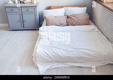 Bedroom interior design with soft orthopedic mattress with pillows, blanket, bed linen, bedding items, gray chest of drawers. Background, backdrop with copy space. Template, mockup for your design. Stock Photo