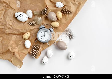 Easter eggs with clock and feathers on a brown kraft paper background on a white table. Top view. For easter greeting cards with copy space. Stock Photo