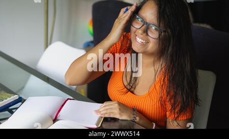 young student sitting at the table studying and holding up her glasses Stock Photo