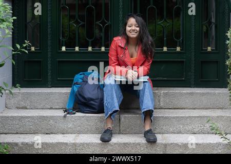 young student sitting on the stairs at the entrance to her home Stock Photo
