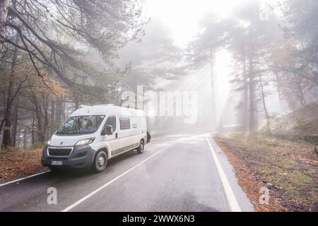 Auf einer kleinen Strasse in einem Wald am Ätna bricht die Morgensonne durch den sich auflösenden Nebel, ein Camper fährt auf der Strasse hinauf zum Vulkan. Catania, Sizilien, Italien Nebelwald am Ätna *** On a small road in a forest on Mount Etna, the morning sun breaks through the dissolving fog, a camper drives up the road to the volcano Catania, Sicily, Italy Cloud forest on Mount Etna Stock Photo