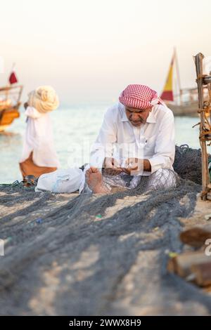 An elderly fishermen in traditional dress fixing his fishing net. Stock Photo