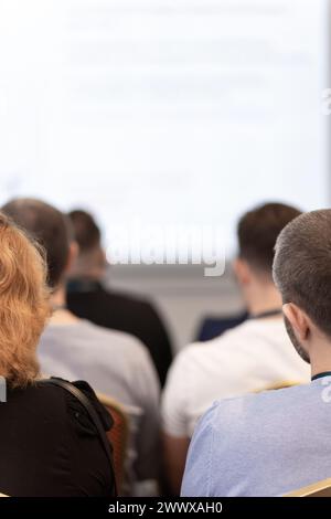 Back view of audience in a business conference or seminar. Audience listens to the lecturer at the conference in auditorium. Stock Photo