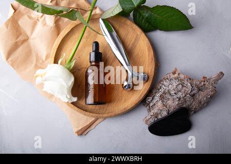 Self care composition with facial serum, gua sha, facial roller. Floral and stone therapy tools for facial rejuvenation on a textured surface. Stock Photo