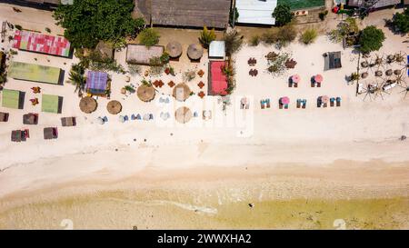 Top down aerial view of various sunshades and resorts along a tropical beach at low tide Stock Photo