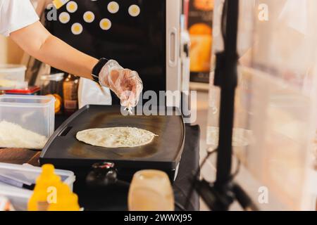 Chef sprinkles a tortilla with cheese preparing fresh quesadilla on ...