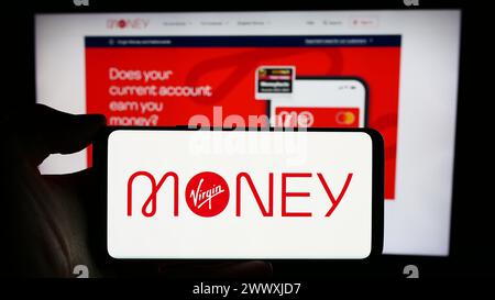 Person holding cellphone with logo of British financial services company Virgin Money in front of business webpage. Focus on phone display. Stock Photo
