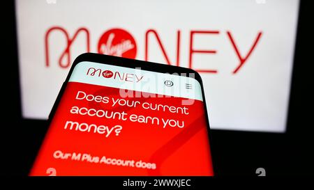 Smartphone with webpage of British financial services company Virgin Money in front of business logo. Focus on top-left of phone display. Stock Photo