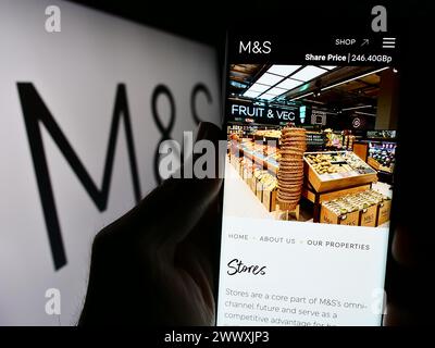 Person holding cellphone with website of British retail company Marks and Spencer Group plc in front of logo. Focus on center of phone display. Stock Photo